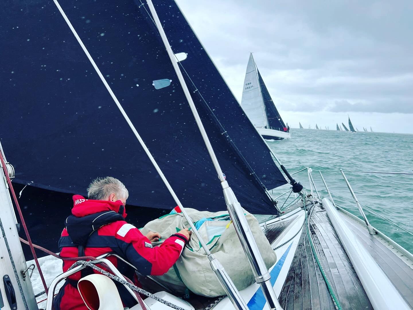 Crew working on deck of SY Cormorant while racing, with the fleet on the water beyond