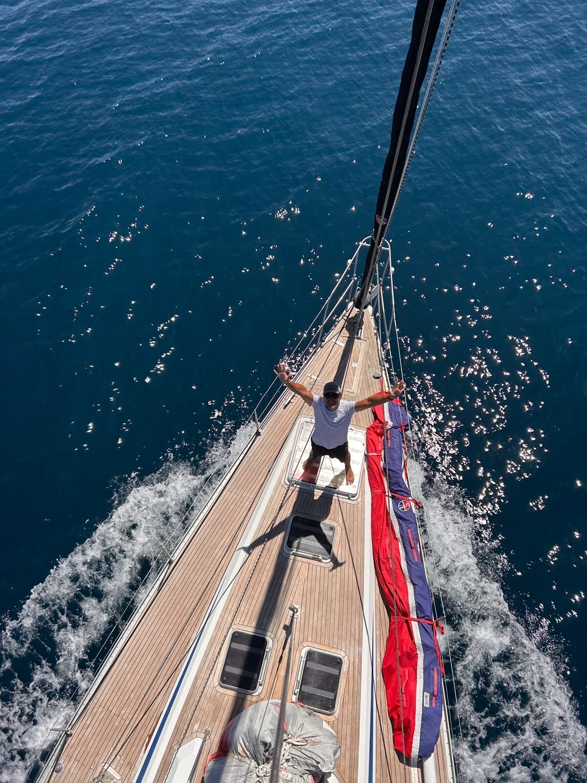 Crew member waving from the foredeck, seen from the top of the mast
